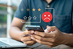 Mann bedient Smartphone, darüber negatives Smiley und schlechte Sterne Bewertung